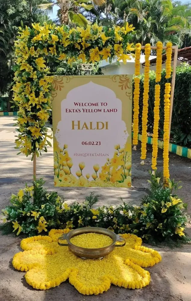 Haldi ceremony decor with marigold garlands, a welcome signboard, and a brass urli on a yellow flower-petal arrangement